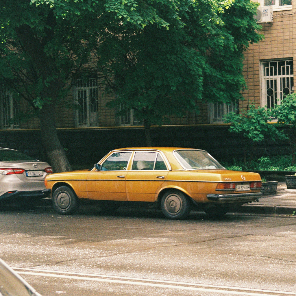 Yellow vintage mercedes parked on a street with trees and buildings in the background. Shot with Sereno Vita f(x) Film Camera